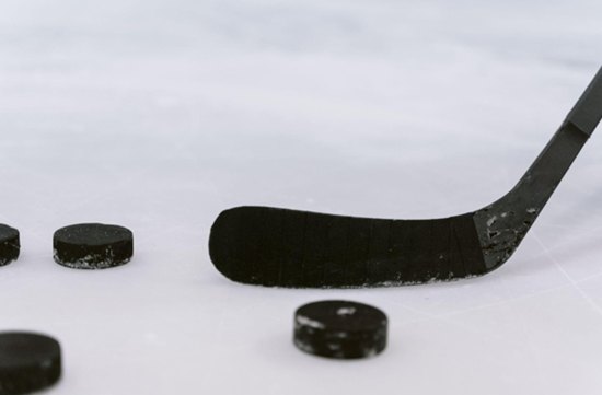 Nahaufnahme eines Eishockeyschlägers und mehrerer schwarzer Pucks auf dem Eis.